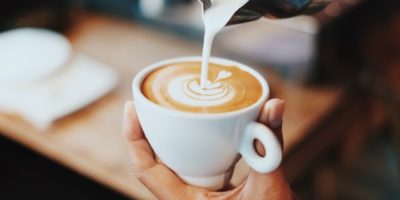 Person pouring milk in coffee cup
