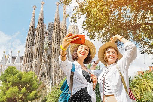 Young girl friends taking a selfie with La Sagrada Família on the background