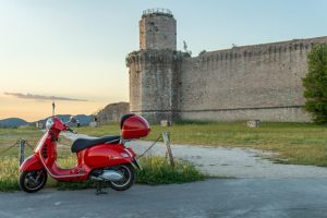 Red Vespa scooter in front of Rocca Maggiore, Assisi