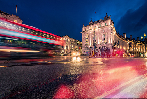 Long exposure photo with evening illumination at Piccadilly Circus in London city during blue hour on a rainy English evening.