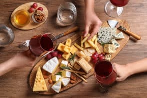 Women with glasses of wine and cheese plate on table, top view